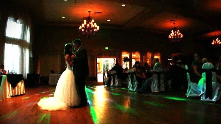 A couple shares their first dance on a beautifully lit dance floor, surrounded by soft, romantic lighting that casts a warm glow over the elegant venue