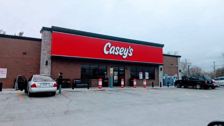 Exterior view of Casey's General Store on California Avenue, Topeka, featuring a red and white storefront with large windows and the familiar Casey's sign. A few cars are parked out front, and bright lighting welcomes customers to the convenience store and gas station.