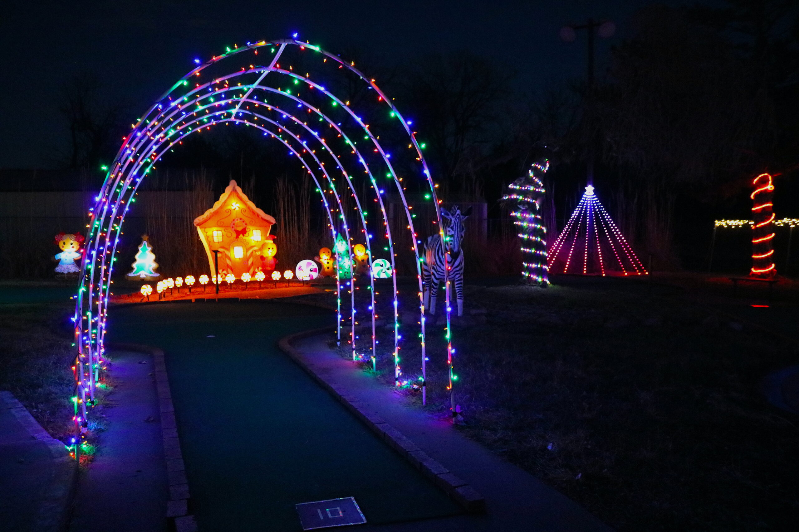 Corner21 Hole 10 featuring a gingerbread house surrounded by vibrant Christmas lights and an illuminated archway, creating a festive holiday atmosphere.