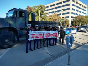 Marines holding a "Toys for Tots" sign, promoting holiday toy donations to help families in need.