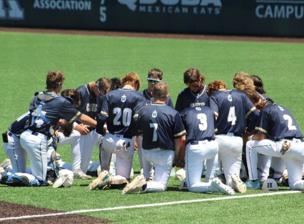 Hayden High School baseball team kneeling in a circle on the field before a game, demonstrating team unity and focus.