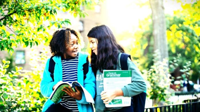 Happy schoolgirls studying together in park by Mary Taylor