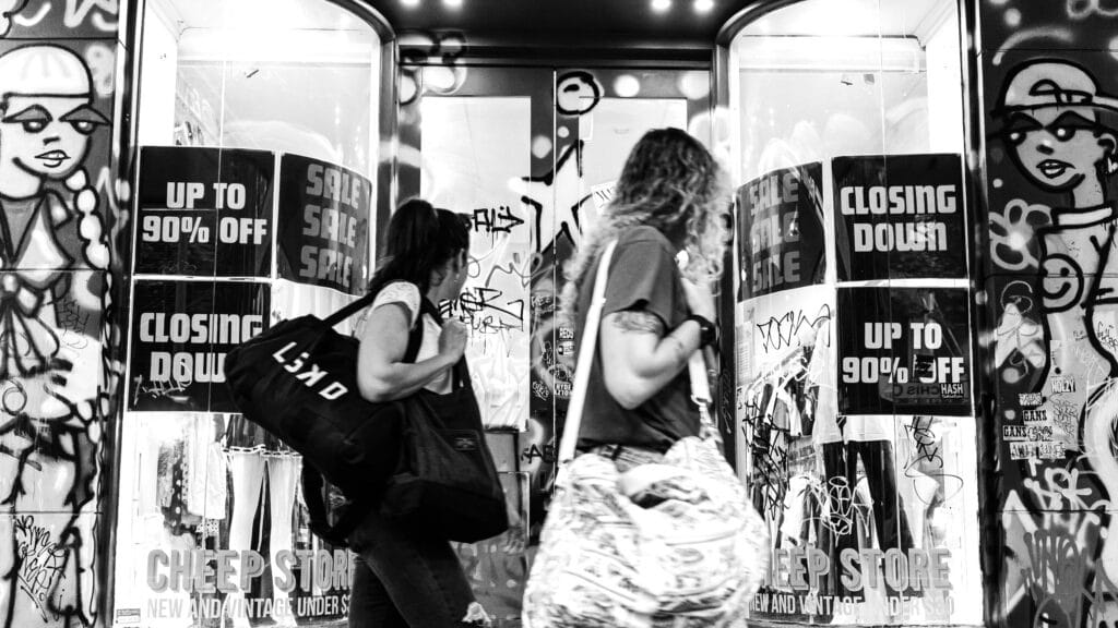 Black and White Photo of Pedestrians Walking Past a Building with Graffiti while shopping by Lawrence Lam